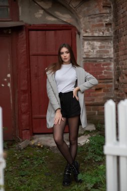 Genç kız bir şehir sokağının arka planında duruyor. Gri montlu kız. Bir esmerle bir dizi fotoğraf.