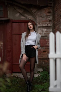 Genç kız bir şehir sokağının arka planında duruyor. Gri montlu kız. Bir esmerle bir dizi fotoğraf.