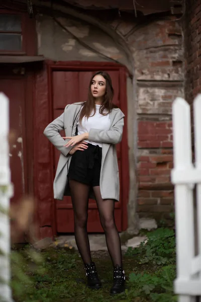 Jeune fille se tient sur le fond d'une rue de la ville. Une fille en manteau gris. Une série de photos avec une brune — Photo