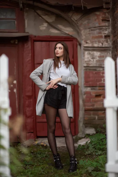 Mladá dívka stojí na pozadí městské ulice. Dívka v šedém kabátě. Série fotek s brunetkou — Stock fotografie
