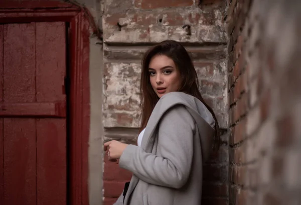 Молода дівчина стоїть на тлі міської вулиці. Дівчинка в сірому пальто. Серія фотографій з брюнеткою — стокове фото