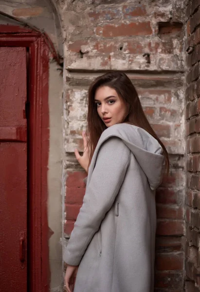 Mladá dívka stojí na pozadí městské ulice. Dívka v šedém kabátě. Série fotek s brunetkou — Stock fotografie