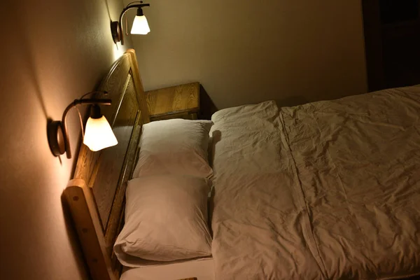 Cama en una habitación de hotel. Cama y almohadas. Una cama con cabecero de madera y dos armarios y lámparas de pie . — Foto de Stock