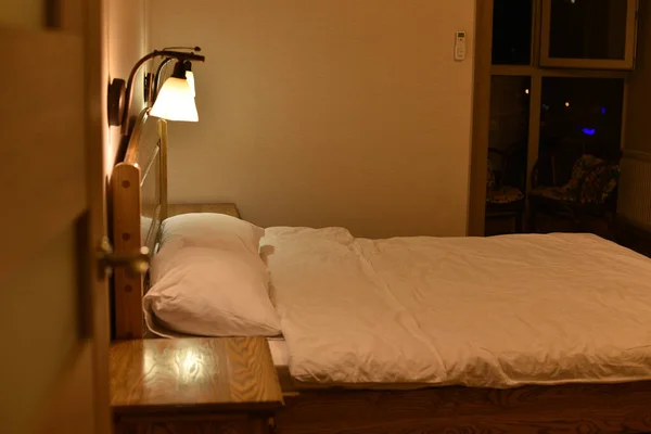 Ліжко в готельному номері. Постіль та подушки. Ліжко з дерев'яним узголів'ям і двома шафами і торшерами . — стокове фото