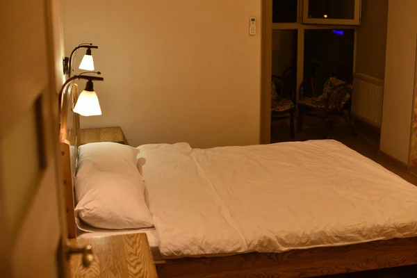 Cama en una habitación de hotel. Cama y almohadas. Una cama con cabecero de madera y dos armarios y lámparas de pie . — Foto de Stock