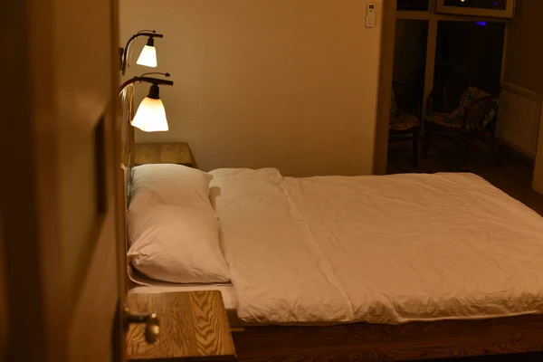 Ліжко в готельному номері. Постіль та подушки. Ліжко з дерев'яним узголів'ям і двома шафами і торшерами . — стокове фото