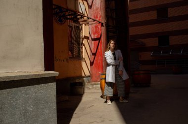 Gri ceketli şık genç güzel kız kameraya bakar ve şehrin arka planına karşı hafifçe gülümser.