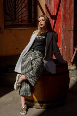 Gri ceketli şık genç güzel kız kameraya bakar ve şehrin arka planına karşı hafifçe gülümser.