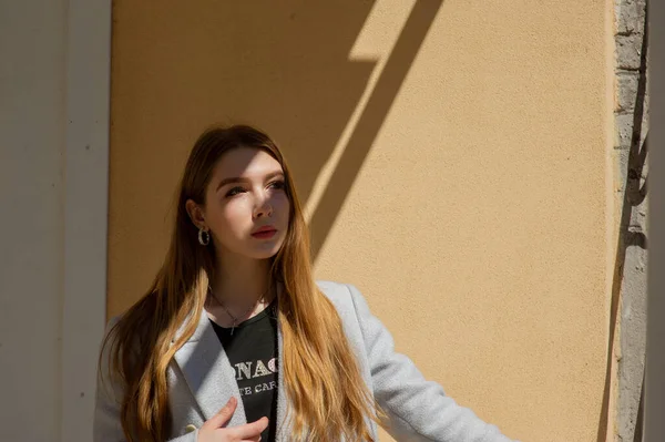 Elegante chica bonita joven con un abrigo gris mira a la cámara y sonríe ligeramente contra el fondo de la ciudad . — Foto de Stock