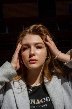 Gri ceketli şık genç güzel kız kameraya bakar ve şehrin arka planına karşı hafifçe gülümser.