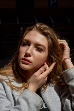 Gri ceketli şık genç güzel kız kameraya bakar ve şehrin arka planına karşı hafifçe gülümser.