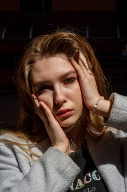 Gri ceketli şık genç güzel kız kameraya bakar ve şehrin arka planına karşı hafifçe gülümser.