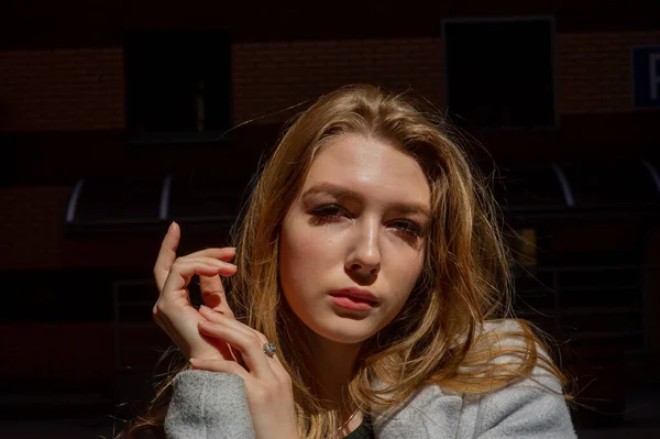 Stylish young pretty girl in a gray coat looks at the camera and smiles slightly against the background of the city. — Stock Photo, Image