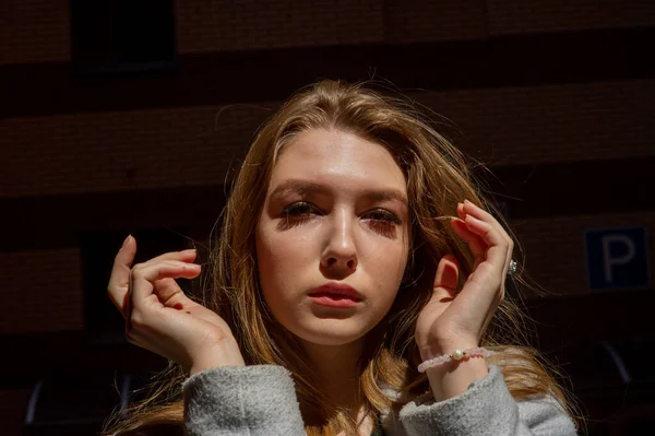 Elegante chica bonita joven con un abrigo gris mira a la cámara y sonríe ligeramente contra el fondo de la ciudad . — Foto de Stock