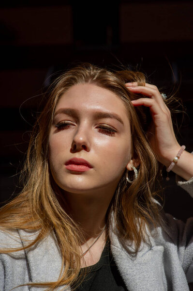 Стильная молодая красивая девушка в сером пальто смотрит в камеру и слегка улыбается на фоне города.
.