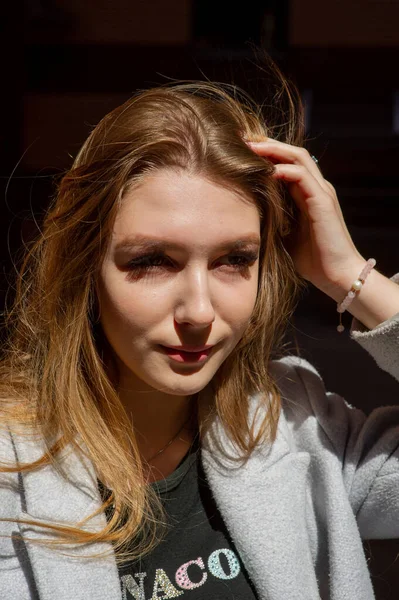 Gri ceketli şık genç güzel kız kameraya bakar ve şehrin arka planına karşı hafifçe gülümser.