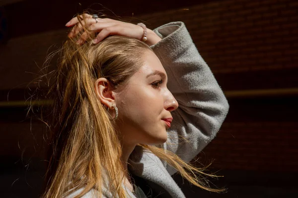 Elegante chica bonita joven con un abrigo gris mira a la cámara y sonríe ligeramente contra el fondo de la ciudad . —  Fotos de Stock