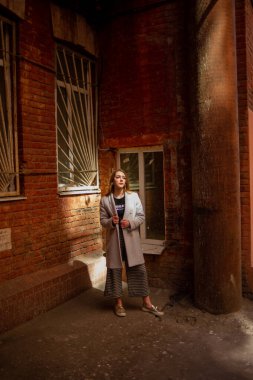 Gri ceketli şık genç güzel kız kameraya bakar ve şehrin arka planına karşı hafifçe gülümser.