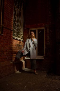 Gri ceketli şık genç güzel kız kameraya bakar ve şehrin arka planına karşı hafifçe gülümser.