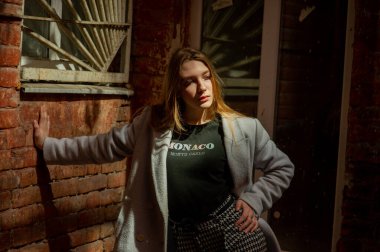 Gri ceketli şık genç güzel kız kameraya bakar ve şehrin arka planına karşı hafifçe gülümser.