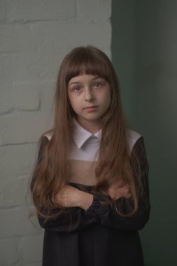 Küçük kız öğrenci ayakta duruyor. 9 yaşında okul elbiseli, kahverengi saçlı bir çocuk..