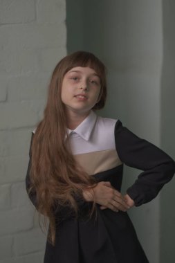 Küçük kız öğrenci ayakta duruyor. 9 yaşında okul elbiseli, kahverengi saçlı bir çocuk..