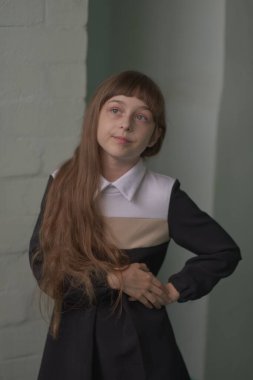 Küçük kız öğrenci ayakta duruyor. 9 yaşında okul elbiseli, kahverengi saçlı bir çocuk..