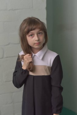 Küçük kız öğrenci ayakta duruyor. 9 yaşında okul elbiseli, kahverengi saçlı bir çocuk..