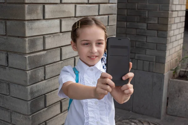 Sorrindo beatiful menina pré-adolescente tomando uma selfie ao ar livre. Criança a tirar um auto-retrato com telemóvel. tecnologia — Fotografia de Stock