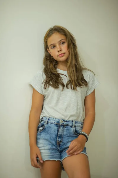 Porträt eines stilvollen jungen schönen Mädchens, das in einem grauen T-Shirt auf weißem Hintergrund lächelt, natürliches Aussehen, lange braune Haare, Jeans, lässiger Stil — Stockfoto