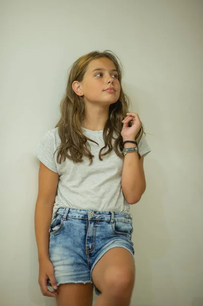Porträt eines stilvollen jungen schönen Mädchens, das in einem grauen T-Shirt auf weißem Hintergrund lächelt, natürliches Aussehen, lange braune Haare, Jeans, lässiger Stil — Stockfoto