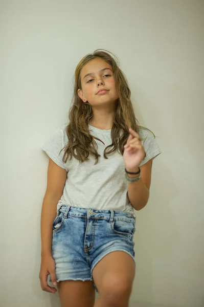 Retrato de uma jovem menina bonita e elegante sorrindo em uma camiseta cinza em um fundo branco, aparência natural, cabelos castanhos longos, jeans, estilo casual — Fotografia de Stock
