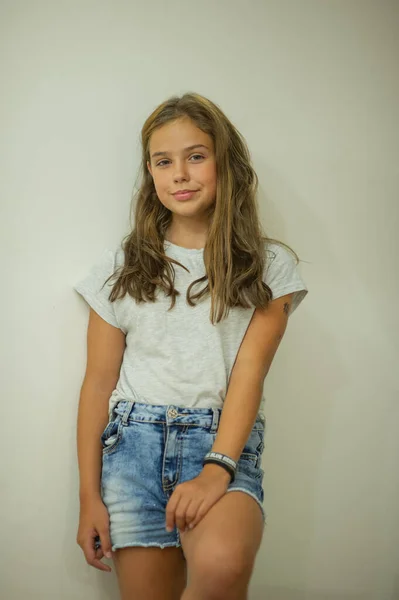 Retrato de uma jovem menina bonita e elegante sorrindo em uma camiseta cinza em um fundo branco, aparência natural, cabelos castanhos longos, jeans, estilo casual — Fotografia de Stock