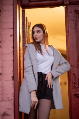 Gri ceketli şık genç güzel kız kameraya bakar ve şehrin arka planına karşı hafifçe gülümser.