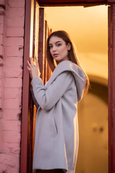 Elegantní Mladá hezká dívka v šedém kabátě hledí na kameru a lehce se usmívá na pozadí města. — Stock fotografie