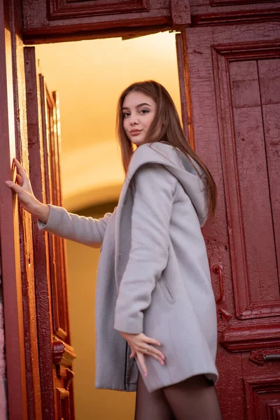 Stylish young pretty girl in a gray coat looks at the camera and smiles slightly against the background of the city. — Stock Photo, Image