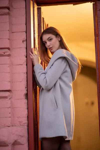 Elegante chica bonita joven con un abrigo gris mira a la cámara y sonríe ligeramente contra el fondo de la ciudad . — Foto de Stock