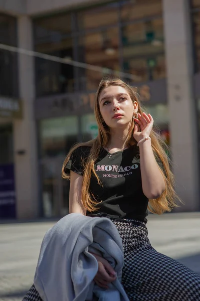 Een jong meisje met een zwart T-shirt en een grijze broek is op straat gefotografeerd. Mooie vrouw op een wandeling in de stad — Stockfoto