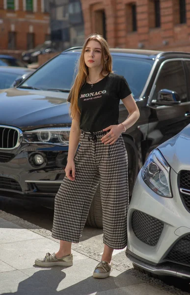 Ένα νεαρό κορίτσι με μαύρο μπλουζάκι και γκρι παντελόνι φωτογραφίζεται στο δρόμο. Όμορφη γυναίκα σε μια βόλτα στην πόλη — Φωτογραφία Αρχείου