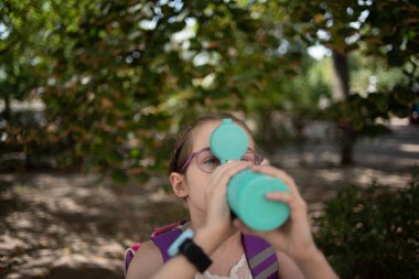 Kupalı kız. Gözlüklü küçük kız termostan ya da termokupadan su içiyor.