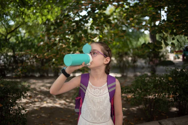 Flicka med kopp. Liten skolflicka i glasögon dricker vatten från en termos eller termomug — Stockfoto