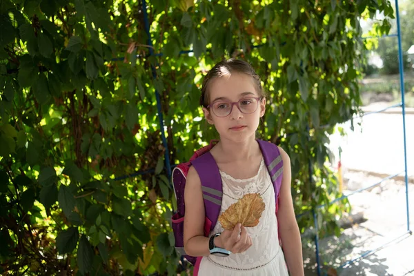 Schulmädchen mit violettem Rucksack und lila Brille. Mädchen im weißen Kleid, trägt im Herbst eine Brille. — Stockfoto