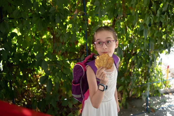 Školačka s fialovým batohem a fialovými brýlemi. Dívka v bílých šatech, nosí brýle na podzim. — Stock fotografie