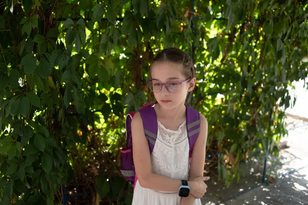 Školačka s fialovým batohem a fialovými brýlemi. Dívka v bílých šatech, nosí brýle na podzim. — Stock fotografie