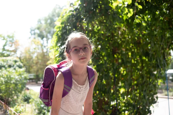 Colegiala con mochila violeta y gafas moradas. Chica en un vestido blanco, con gafas en otoño . — Foto de Stock