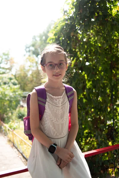 Colegiala con mochila violeta y gafas moradas. Chica en un vestido blanco, con gafas en otoño . — Foto de Stock