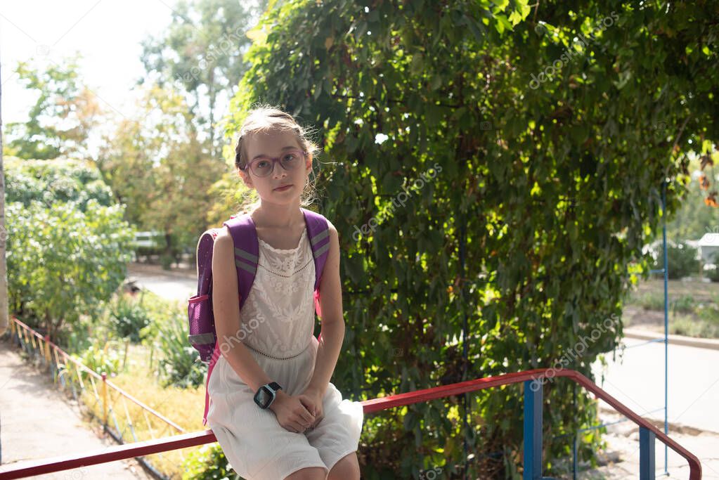 Schoolgirl with a violet rucksack and purple glasses. Girl in a white dress, wearing glasses in autumn.