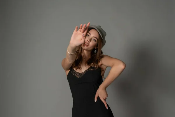 Glamoroso jovem mulher usa vestido elegante posando com cabelo agitado na parede cinza — Fotografia de Stock