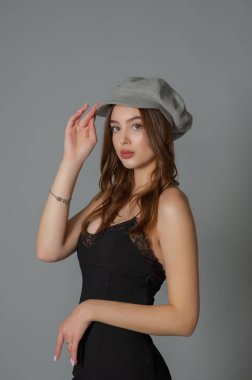 Göz kamaştırıcı genç kadın, gri duvarda dalgalı saçlarla poz veren şık elbiseler giyiyor.