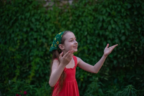 Little girl on the street against a background of green foliage. Girl with long hair. Child 9-10 years old — 스톡 사진